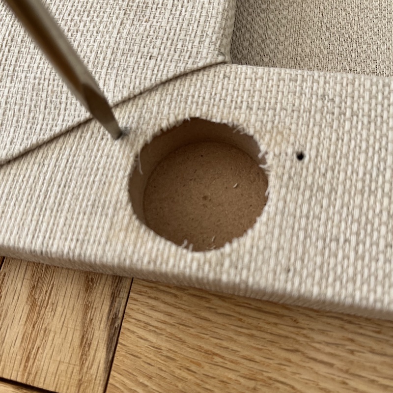 ネジ穴部分の布にドライバーの先を入れて穴を開けているところ